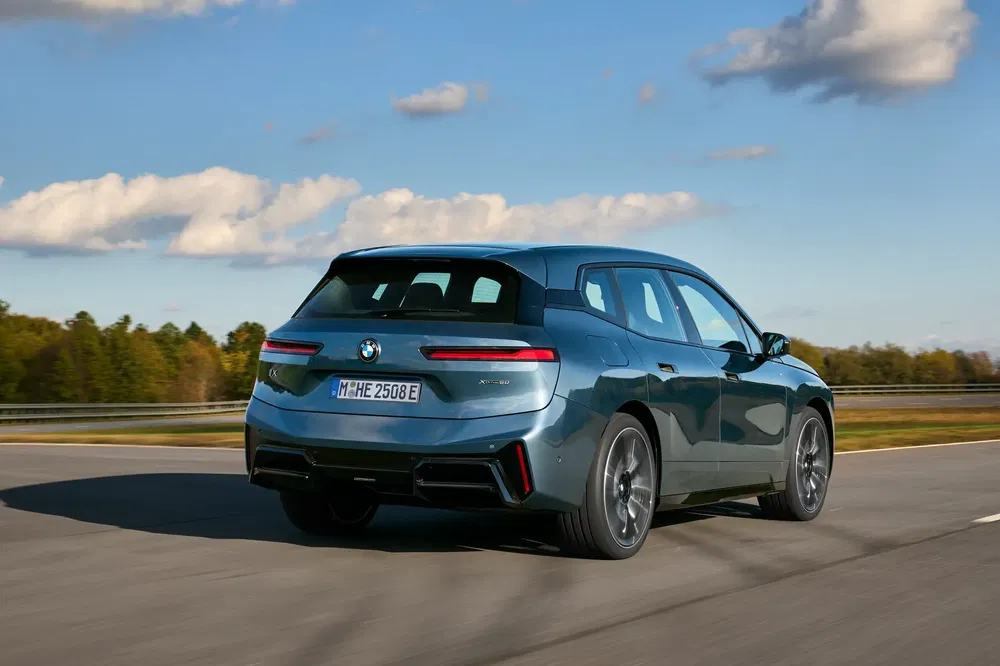 BMW iX elektrische auto op straat, donkerkleurige carrosserie tegen blauwe lucht.