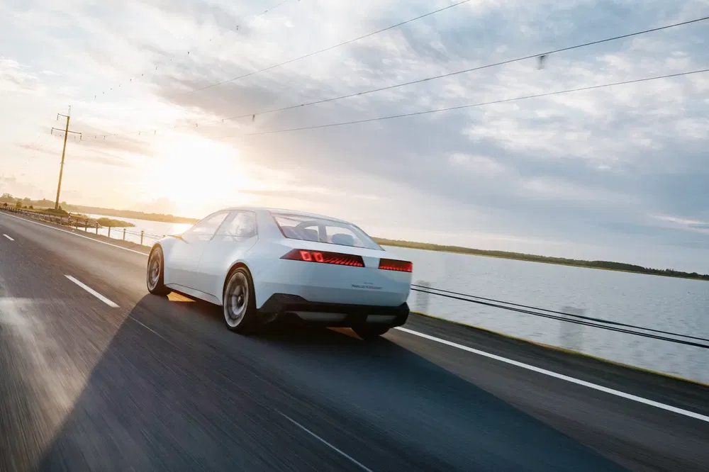 Prototype de voiture électrique Hyundai roulant sur une route côtière au coucher du soleil.