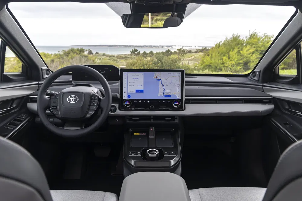 Moderne Toyota-interieur met touchscreen en multifunctioneel stuur, panoramisch uitzicht buiten.