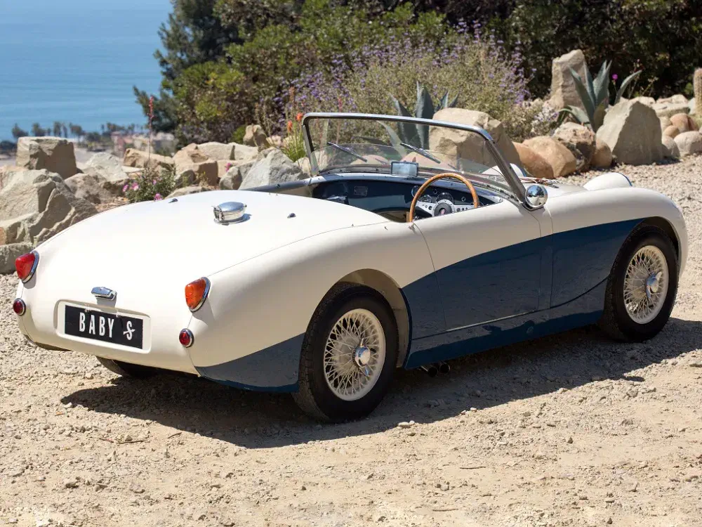 Austin Healey Sprite classique en plein air sur route de campagne ensoleillée.