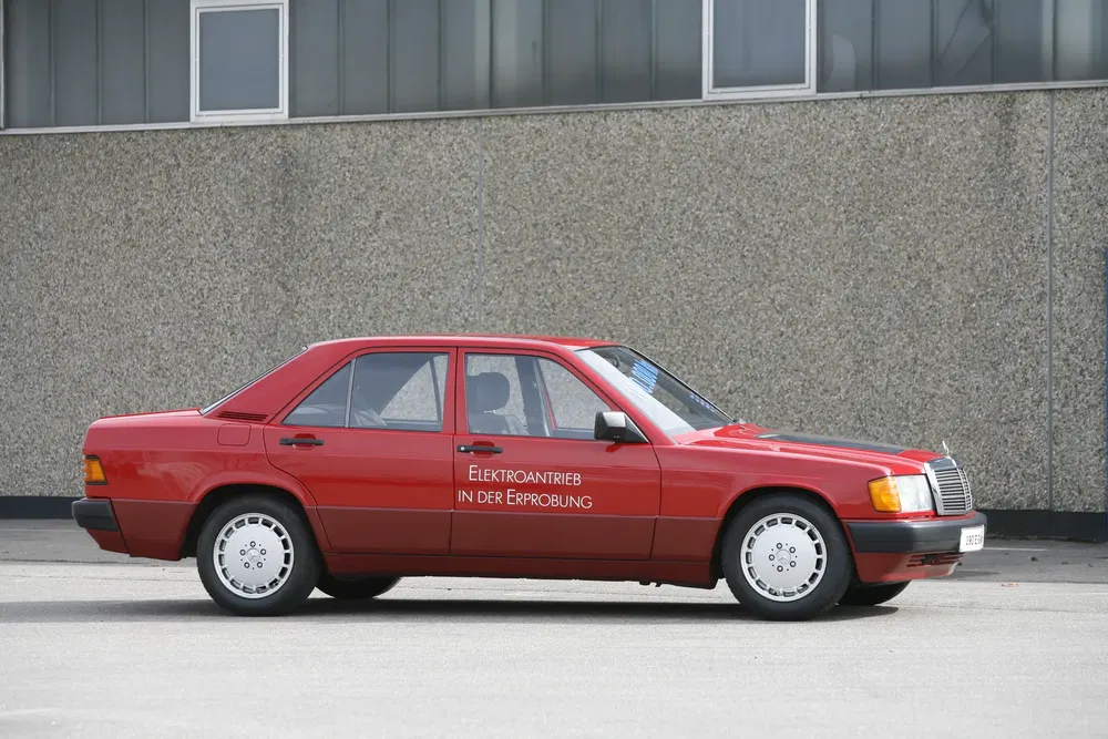 Mercedes-Benz 190 électrique rouge, stationné devant un bâtiment industriel.