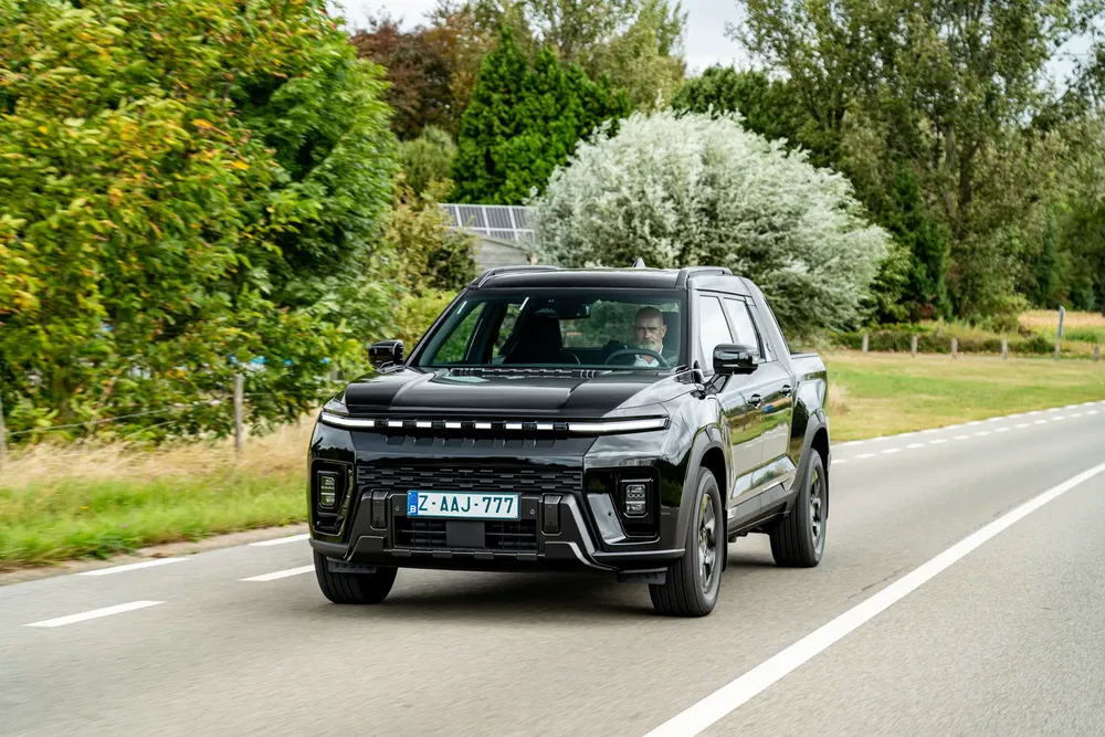 Pickup noir moderne sur une route de campagne bordée d'arbres feuillus.