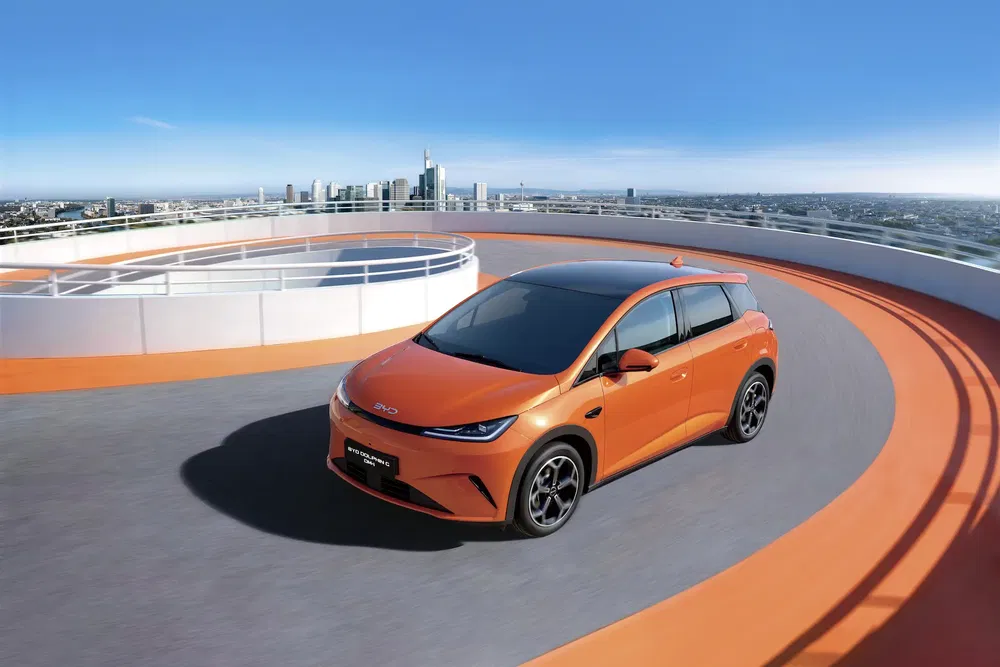 Voiture électrique BYD orange sur un circuit en ville avec horizon urbain.