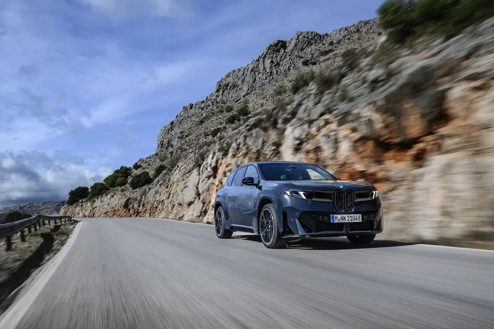 BMW iX en mouvement sur route de montagne sinueuse, ciel dégagé en arrière-plan.