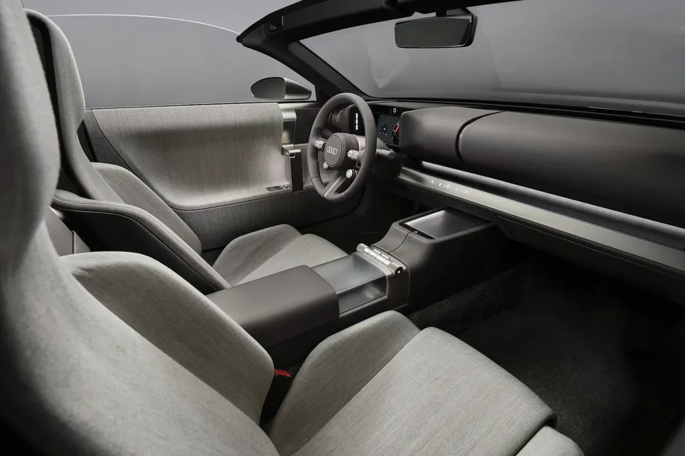 Futuristisch interieur van Audi-auto met grijze stoffen stoelen en minimalistisch dashboard.
