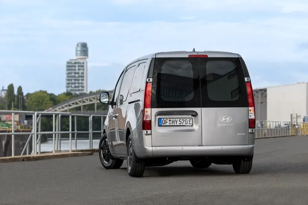 Hyundai Staria électrique gris sur route, arrière-plan urbain moderne.