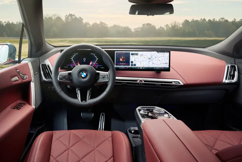 Interieur van BMW met digitaal dashboard en stijlvolle rode lederen stoelen.