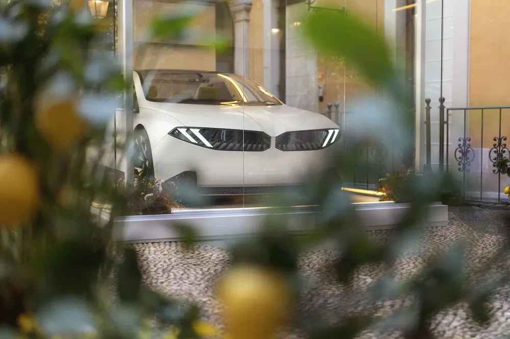 Voiture concept BMW blanche vue derrière plantes, exposée dans une vitrine élégante.