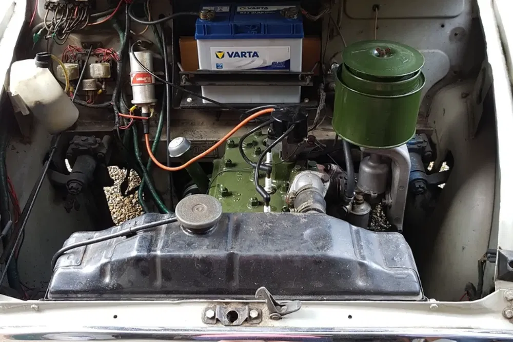 Moteur ancien d'une voiture classique avec batterie Varta, câbles et pièces mécaniques visibles.