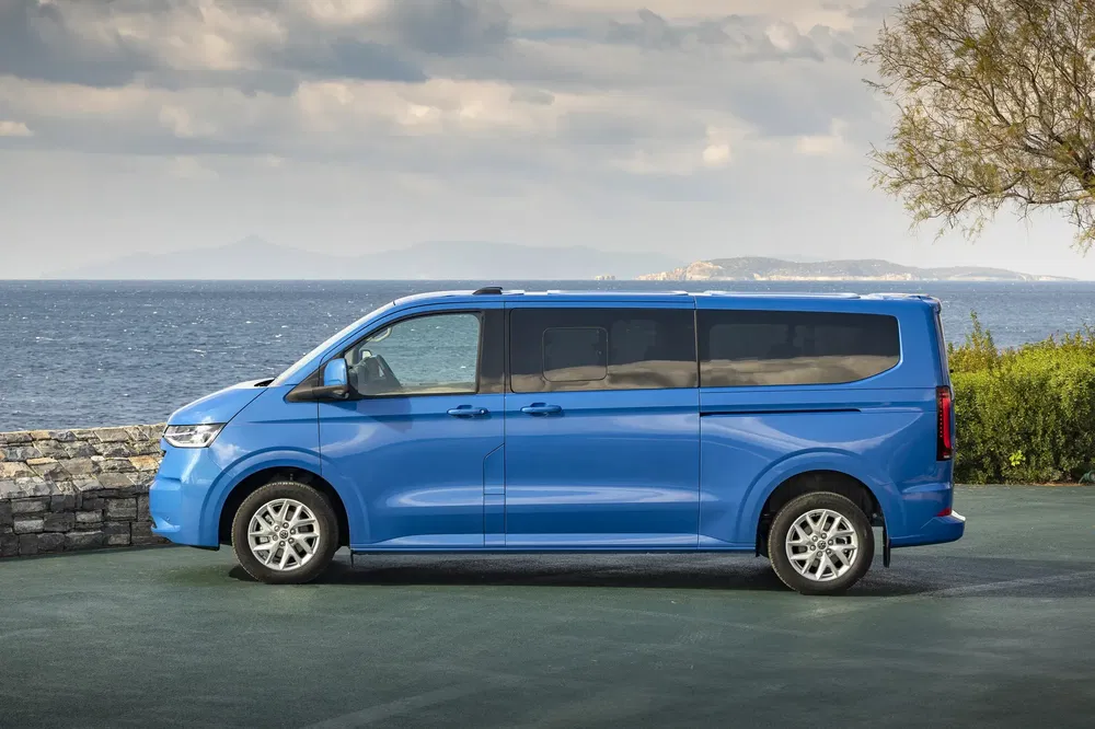 Blauwe Hyundai Staria bestelwagen geparkeerd bij zee met bewolkte lucht op de achtergrond.
