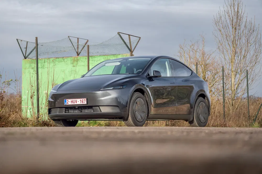 {"fr":"Tesla Model Y gris garé devant une clôture verte sur une route rurale.","nl":"Grijze Tesla Model Y geparkeerd voor groene afrastering op een landelijke weg."}