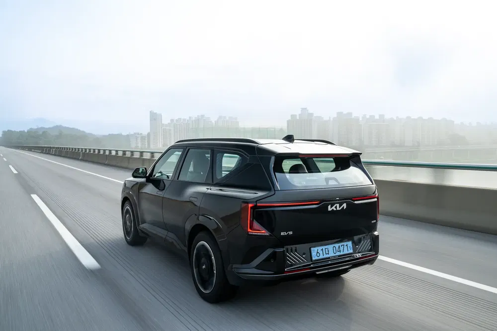 Kia EV5 noire sur autoroute, design moderne, arrière distinctif, skyline urbaine en arrière-plan.