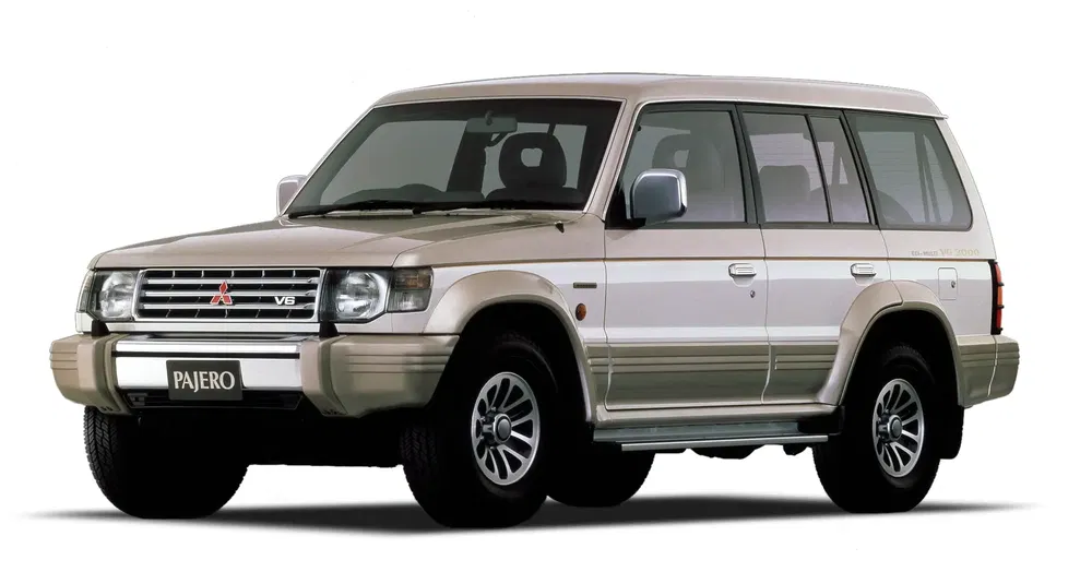 SUV Mitsubishi Pajero V6 beige, zijaanzicht op witte achtergrond.