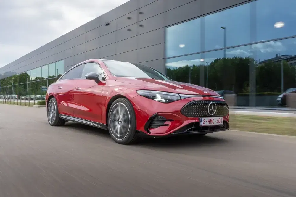 Mercedes rouge passant devant un bâtiment moderne avec des reflets vitrés, style élégant.
