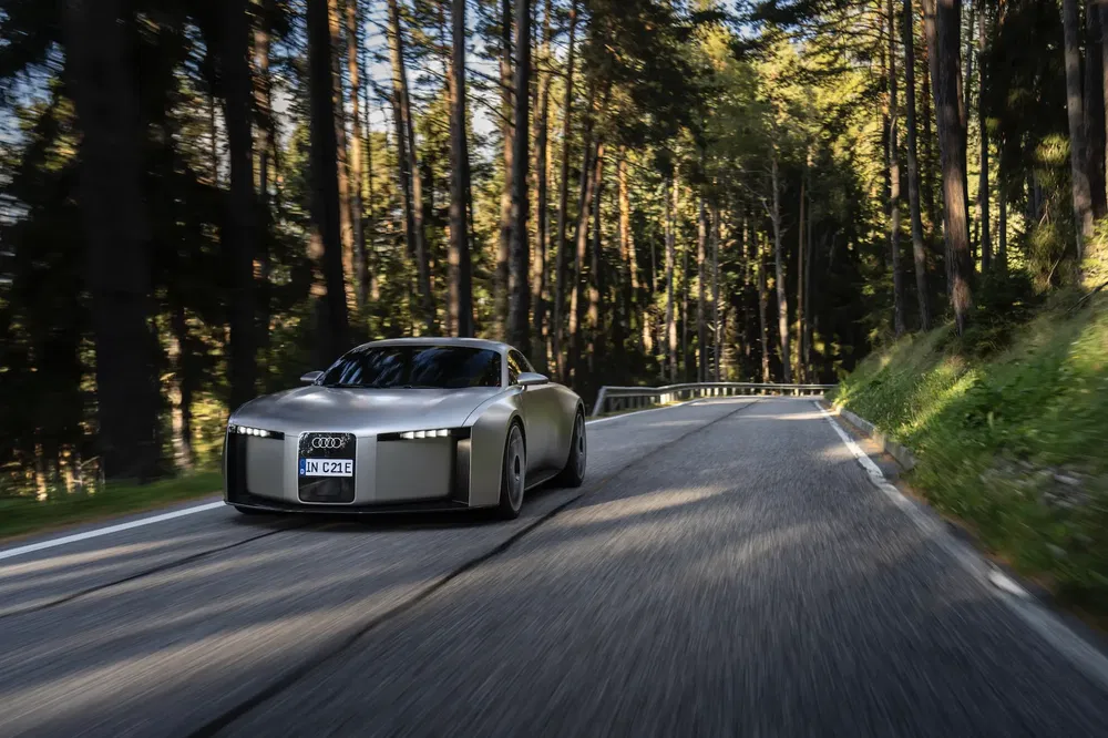 Audi concept car futuriste roulant sur une route forestière pittoresque ensoleillée.
