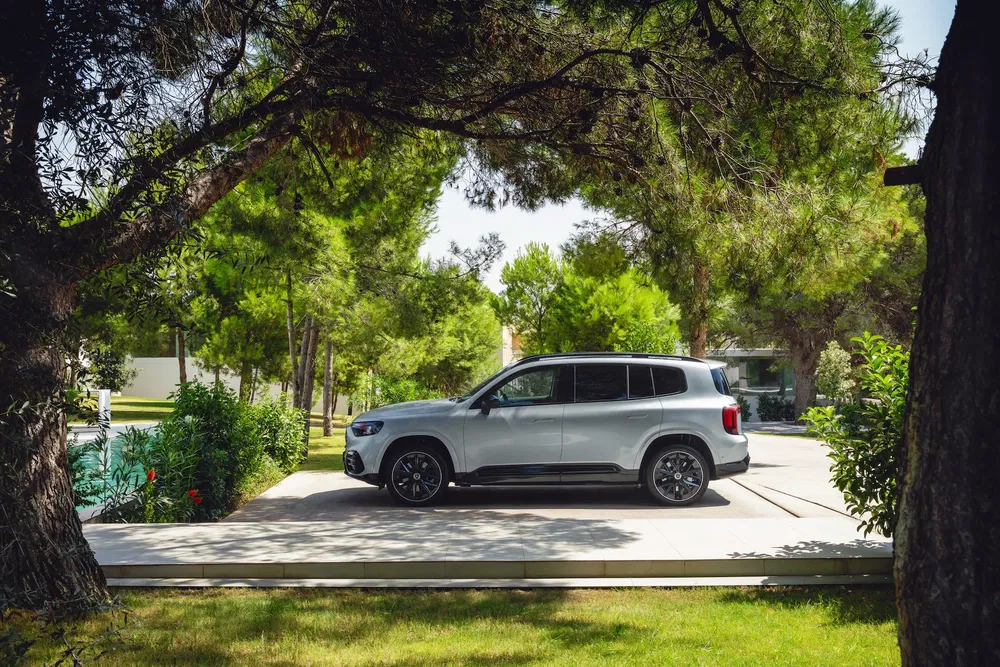 Mercedes GLB argent garée sous des arbres, arrière-plan de jardin verdoyant.