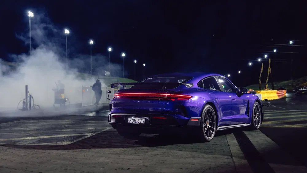 Voiture Porsche au départ d'une course, éclairage nocturne saisissant et fumée en arrière-plan.
