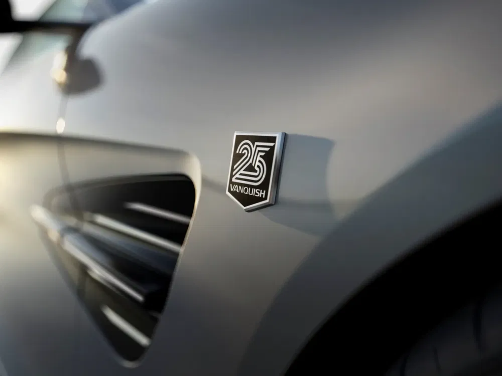 {"fr":"Détail du badge \"25 Vanquish\" sur une Aston Martin grise en gros plan.","nl":"Detail van de \"25 Vanquish\" badge op een grijze Aston Martin van dichtbij."}