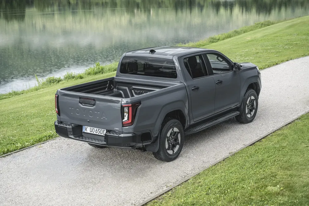 Toyota pick-up gris sur chemin en gravier près d'un lac verdoyant.
