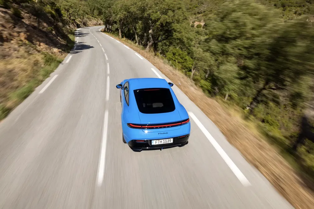 Blauwe Alpine A110 op kronkelige weg omgeven door bomen, dynamische achteraanzicht.