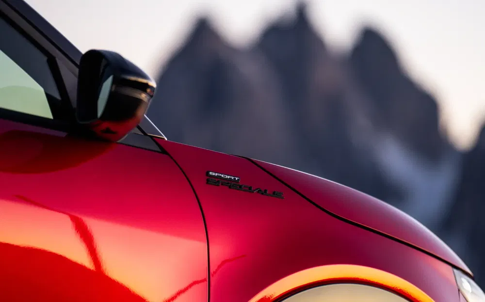 Gros plan d'une voiture rouge Alfa Romeo avec badge "Sport Speciale" devant montagnes floues.