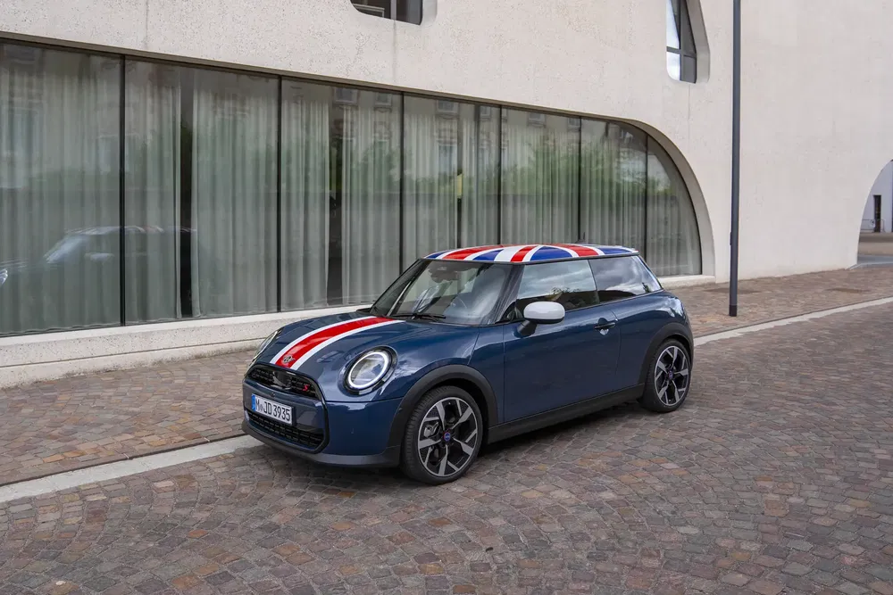 Mini Cooper bleu avec toit et capot aux couleurs britanniques, stationné sur rue pavée.