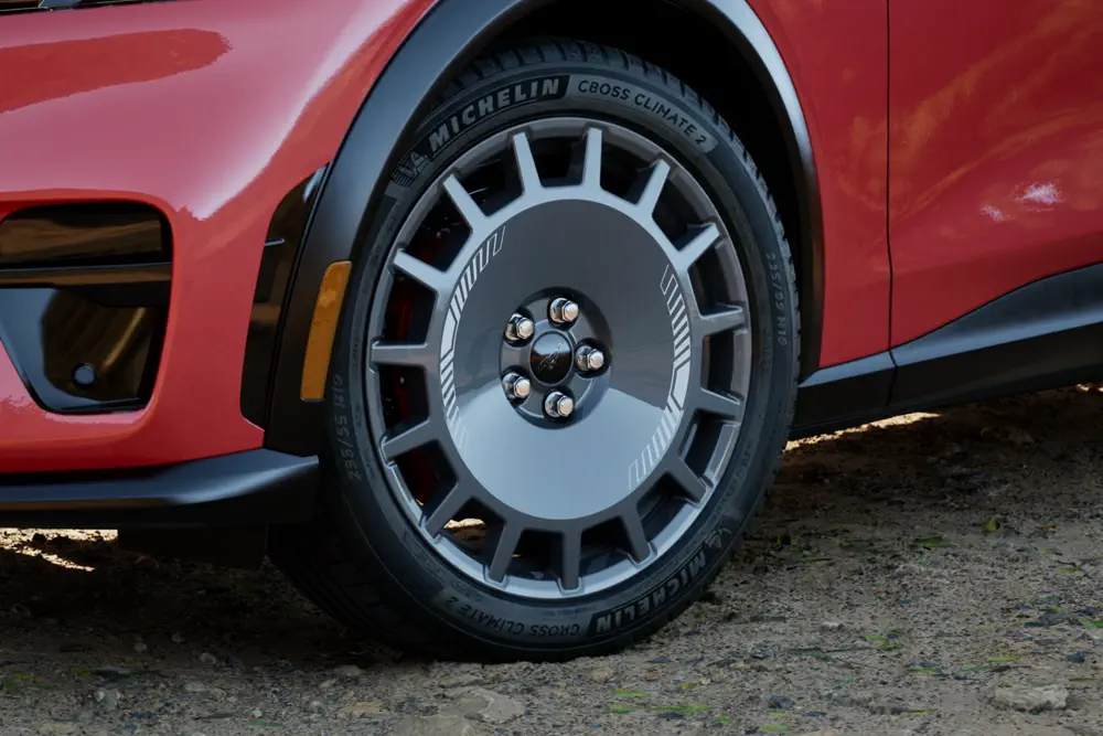 Roue de voiture électrique avec pneu Michelin CrossClimate 2 sur fond de carrosserie rouge.
