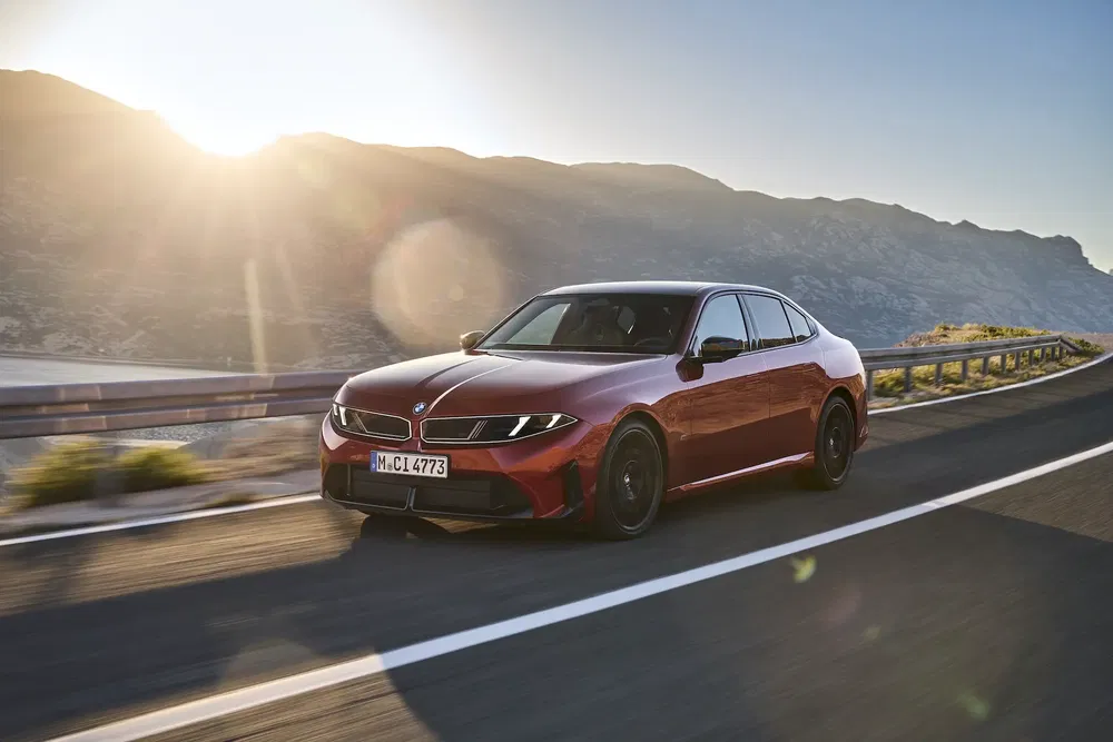 BMW série 3 rouge roulant sur une route côtière ensoleillée.