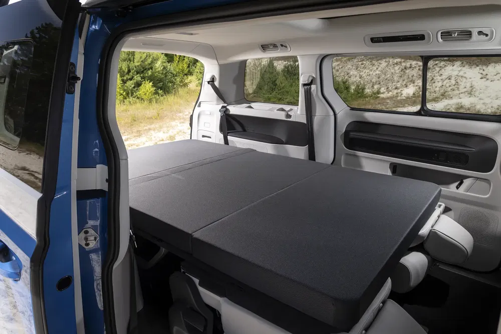 Intérieur d'un Volkswagen Caddy avec les sièges arrière transformés en lit pour camping.