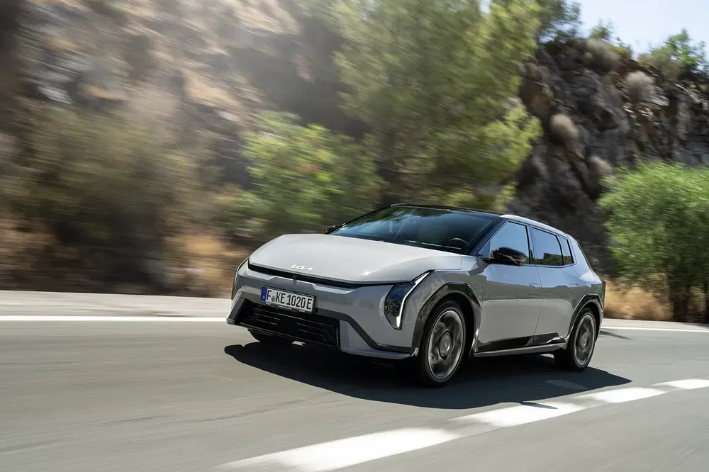Kia EV9 roulant sur une route bordée d'arbres, design moderne et sportif.