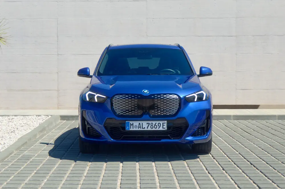 Blauwe BMW X1 geparkeerd op een zonnige parkeerplaats, met stijlvolle voorzijde.