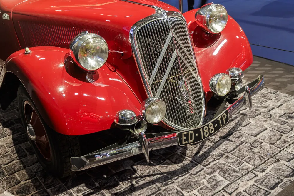 Citroën Traction Avant rouge exposée sur un sol pavé, mettant en valeur son design classique.