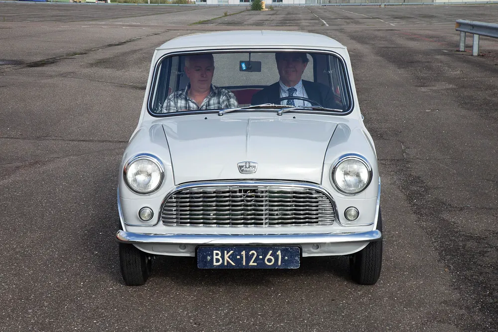 Witte klassieke Mini Cooper met twee personen binnen op een verlaten weg.