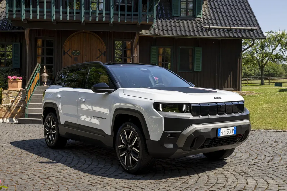 Jeep Compass blanche garée devant une maison rustique avec un toit en tuiles.