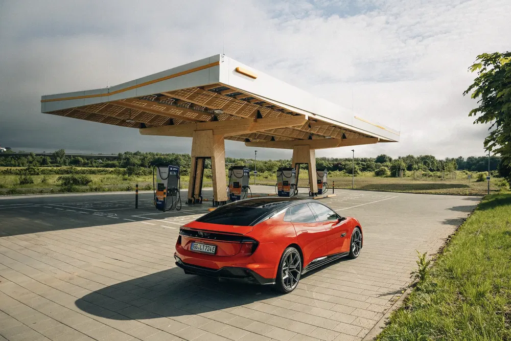 Voiture électrique rouge à une station de recharge moderne sous un ciel nuageux.