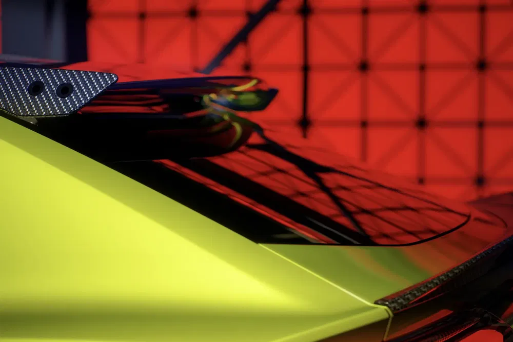 Aileron carbone d'une voiture jaune contre une grille rouge moderne.