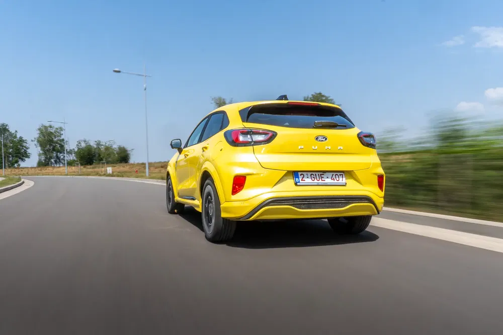 Felle gele Ford Puma op een bochtige weg onder een blauwe hemel.