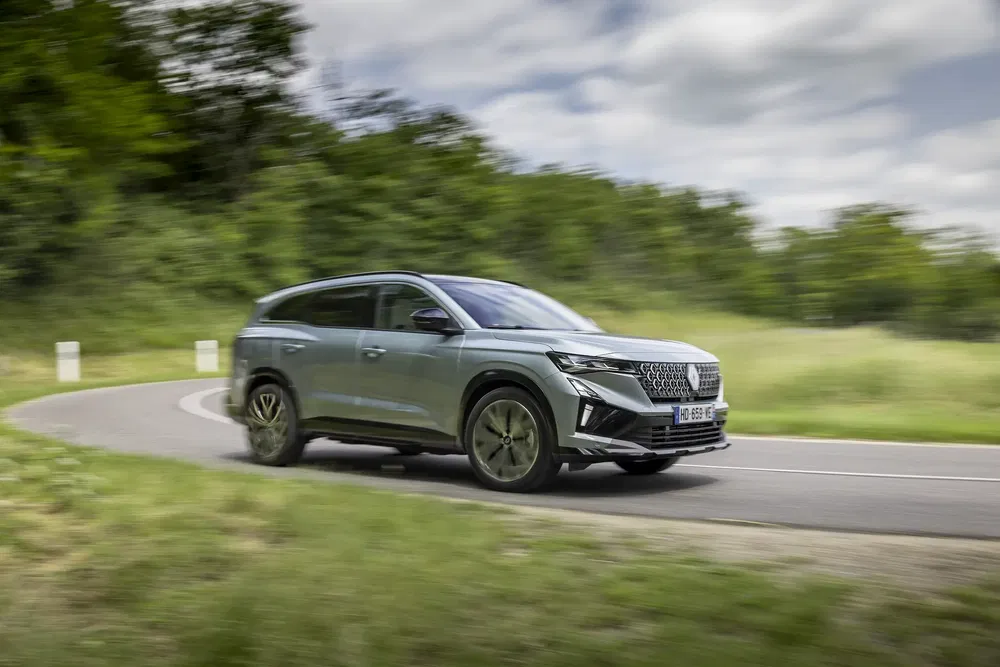 Renault Espace SUV rijdt op een bochtige weg omgeven door groen.