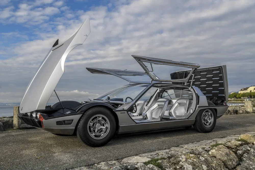 Retroconceptauto met geopende deuren en motorkappen tegen een bewolkte achtergrond.