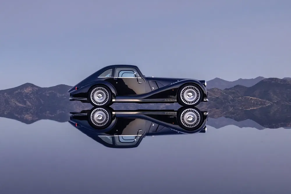 Voiture Morgan Aero 8 noire reflétée sur surface lisse avec montagnes en arrière-plan.