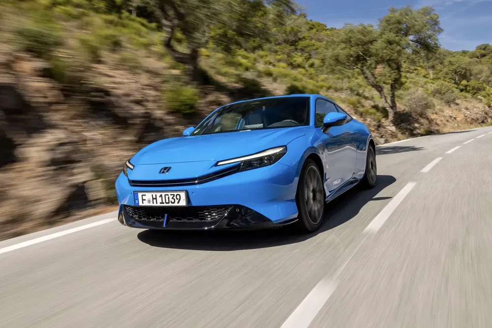 Nieuwe blauwe Honda Civic rijdt op kronkelige weg met struiken en bomen langs de kant.
