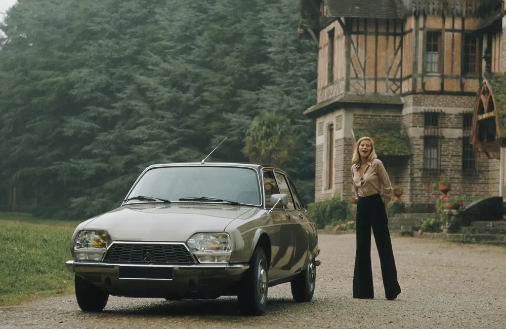 Citroën GS classique devant un manoir, entouré de végétation luxuriante.