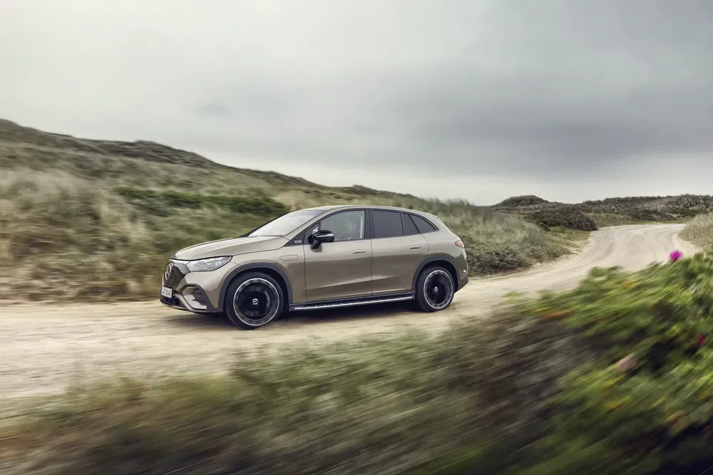 Mercedes-Benz EQE SUV rijdt op kronkelige landweg onder bewolkte hemel.
