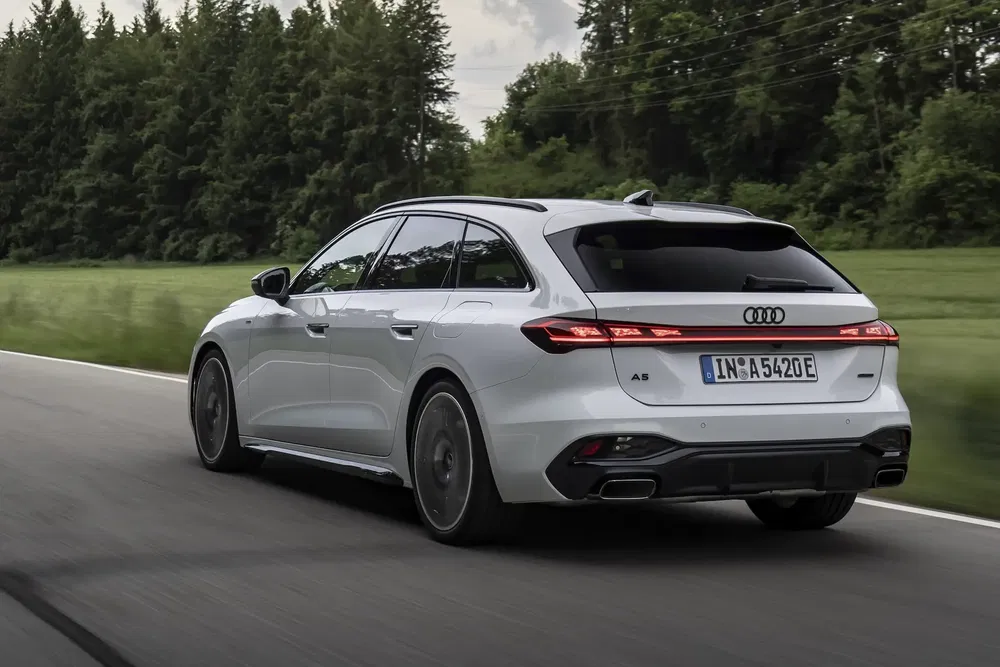 Witte Audi A6 op weg omringd door bos, strak en modern ontwerp.