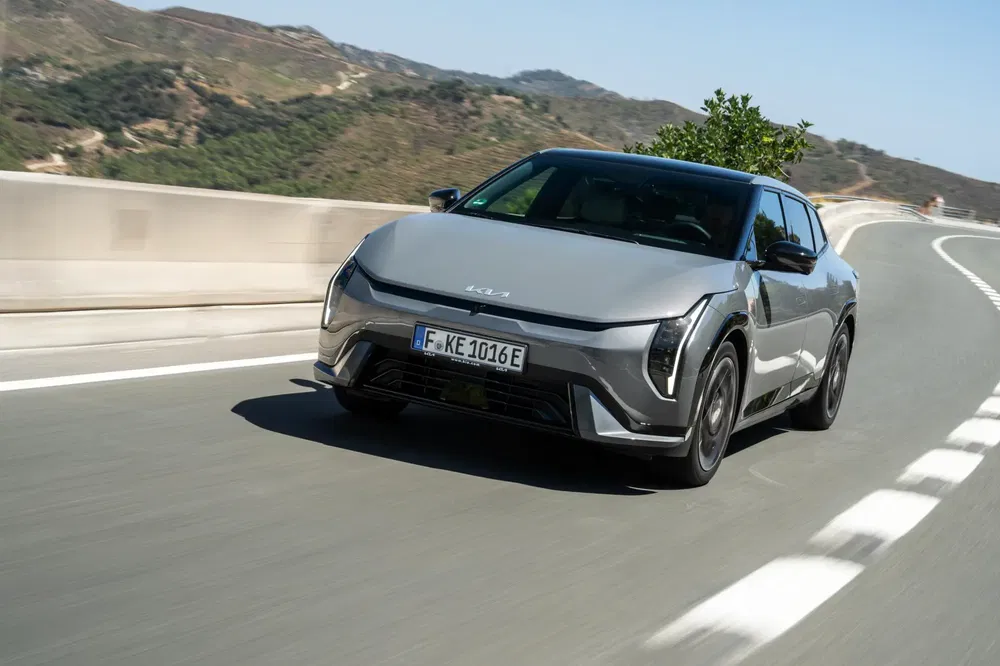 Grijze Kia EV9 op een kronkelige weg met heuvels op de achtergrond.