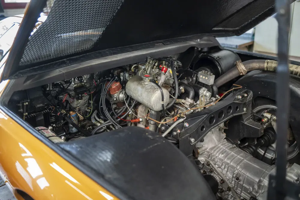 Moteur de voiture de sport rétro sous capot ouvert, détails mécaniques apparents.