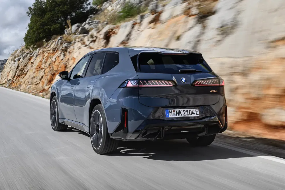 BMW iX gris roulant sur une route montagneuse, vue arrière dynamique et élégante.