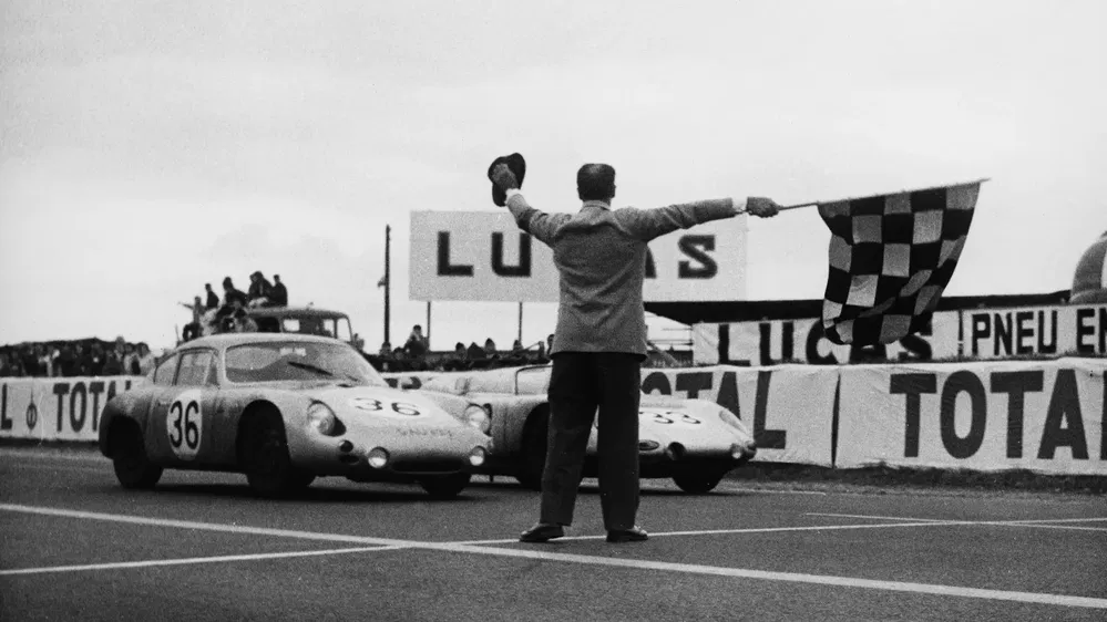 Voiture de course historique Porsche franchissant la ligne d'arrivée, drapeau à damier agité.