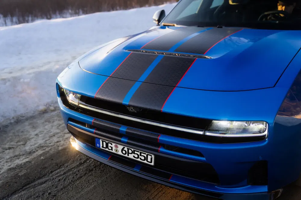 Avant d'une Dodge Charger électrique bleue avec bandes noires sur route enneigée.