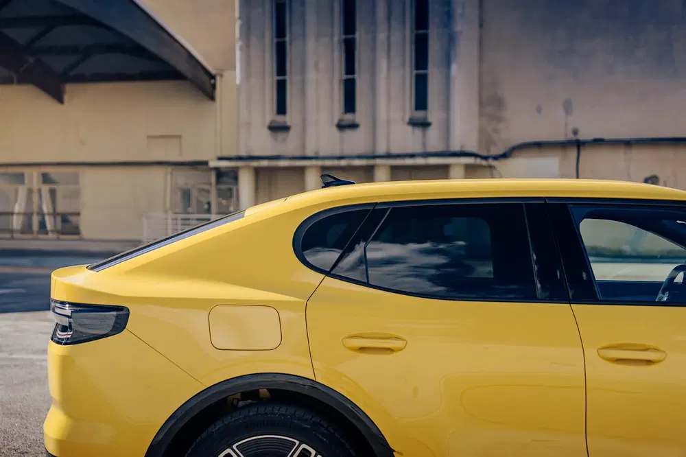 Vue latérale d'une voiture jaune élégante devant un bâtiment industriel, ciel reflété.